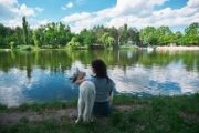 Best friends, woman hugging a dog, resting while enjoying the amazing view of landscape, lake reflecting the sky and trees. Back view.